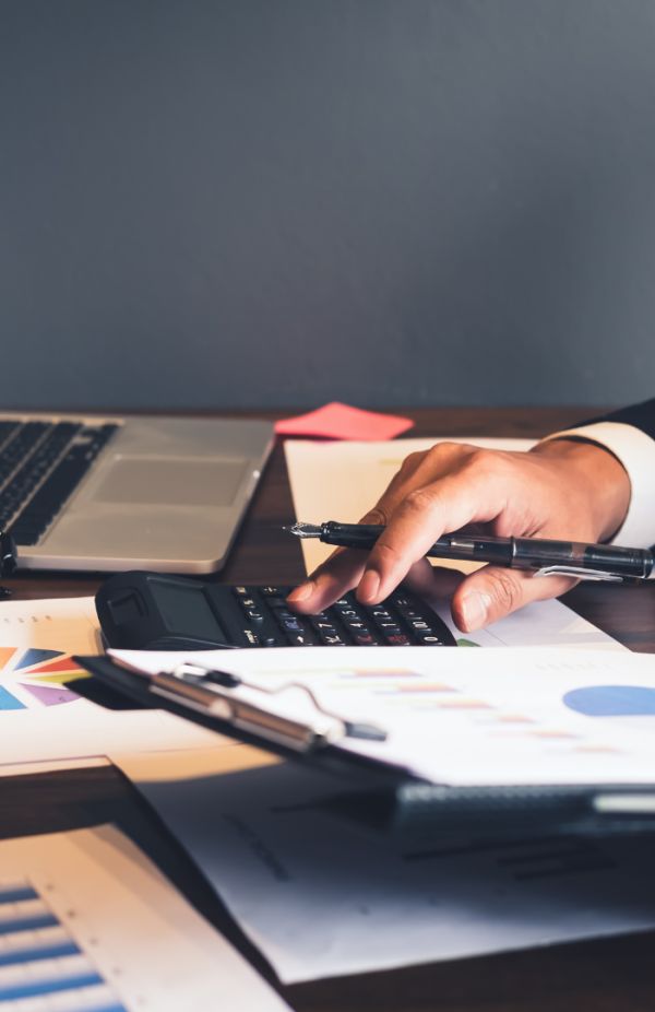 Un avocat en chemise claire, assis à un bureau, écrit sur un document avec un ordinateur portable ouvert et des dossiers autour, dans un environnement de travail professionnel.