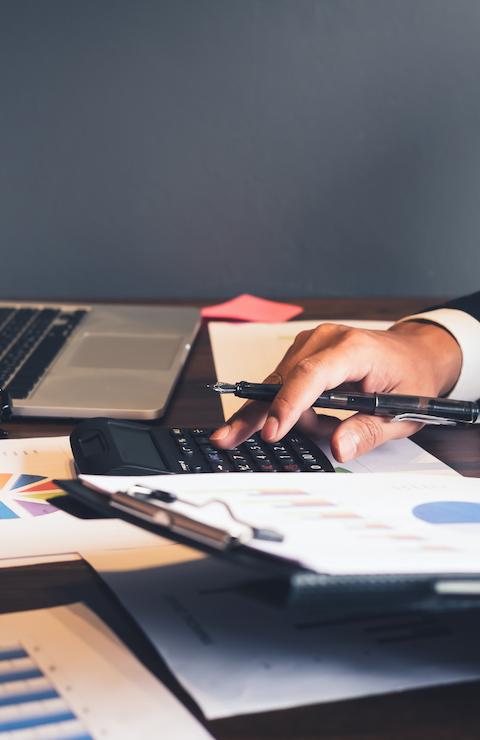 Un avocat en chemise claire, assis à un bureau, écrit sur un document avec un ordinateur portable ouvert et des dossiers autour, dans un environnement de travail professionnel.